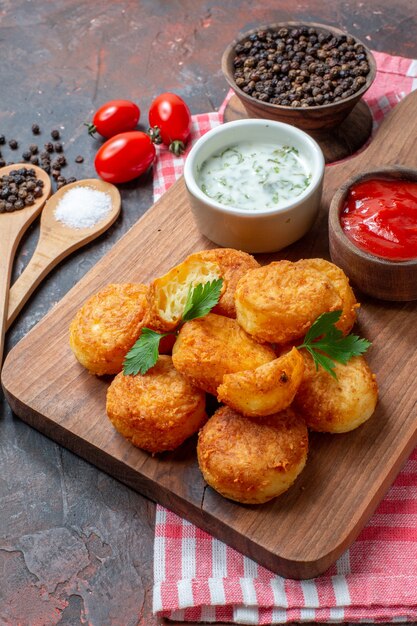 Ansicht von unten Chicken Nuggets auf Holzbrett mit Saucen Kirschtomaten Holzlöffel schwarzer Pfeffer in Schüssel auf dunklem Hintergrund