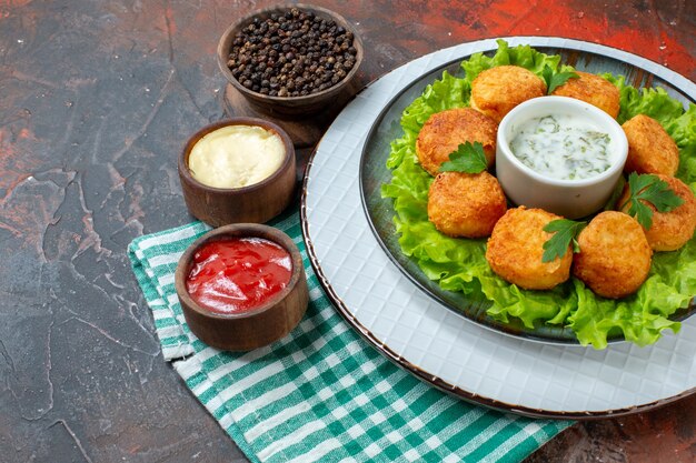 Ansicht von unten Chicken Nuggets Salat und Sauce auf Teller schwarzer Pfeffer in Schüssel Saucen in kleinen Schüsseln auf dunklem Tisch