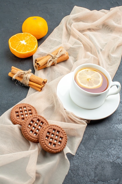 Ansicht von unten eine Tasse Tee mit Zitronen-Zimt-Sticks Kekse auf beigem Schal orange auf dunkler Oberfläche