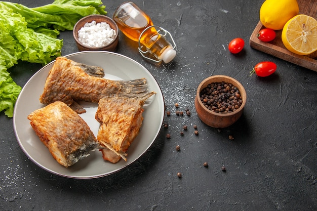 Ansicht von unten Fisch braten auf Teller Salat schwarzer Pfeffer und Meersalz in Schalen Kirschtomaten Zitronen auf Holzbrett auf schwarzem Tisch