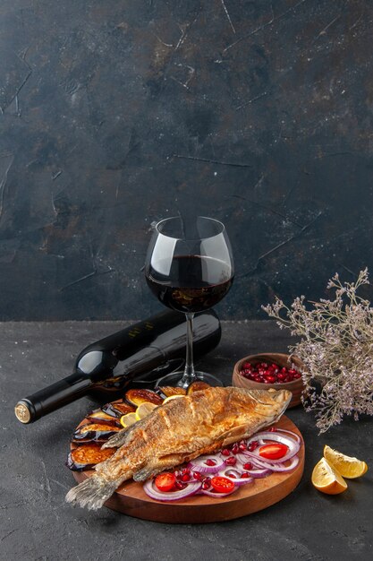 Ansicht von unten Fisch braten gebratene Auberginen geschnittene Zwiebel auf Holz Servierbrett Weinflasche und Glas auf dunklem Hintergrund Freiraum