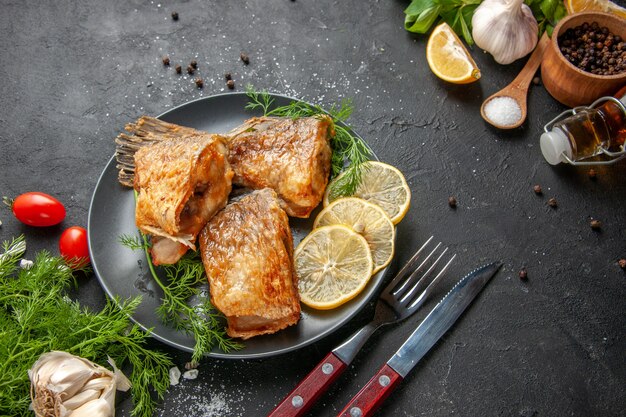 Ansicht von unten Fisch braten schwarzen Pfeffer in Schüssel Minze Zitronenscheiben Gabel und Messer auf schwarzem Tisch