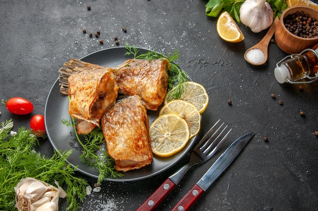 Ansicht von unten Fisch braten schwarzen Pfeffer in Schüssel Minze Zitronenscheiben Gabel und Messer auf schwarzem Tisch