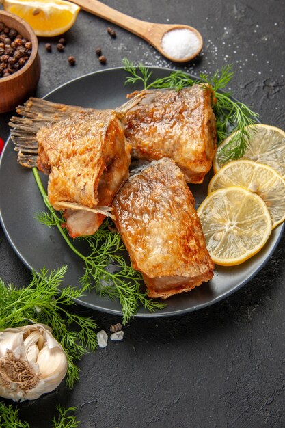 Ansicht von unten Fisch braten schwarzen Pfeffer in Schüssel Minze Zitronenscheiben Holzlöffel auf schwarzem Tisch