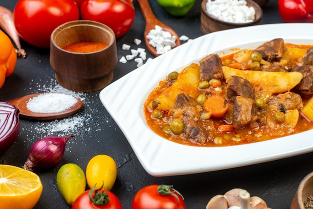 Ansicht von unten Fleischsuppe mit Garnitur Salz in Holzlöffel Gewürze in kleinen Schüsseln Tomaten cumcuats auf schwarzem Tisch