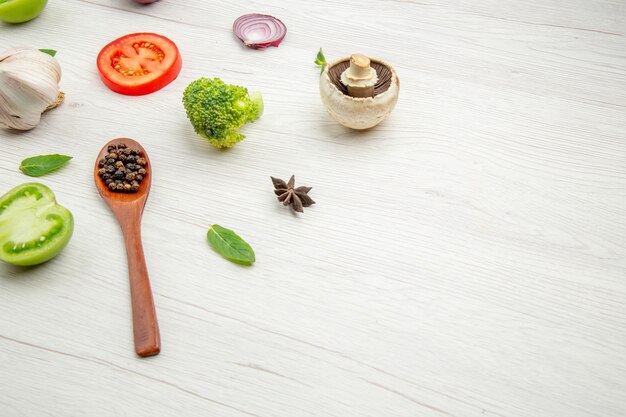 Ansicht von unten frisch geschnittenes Gemüse Holzlöffel mit schwarzen Pfeffer Pilzen grüne und rote Tomaten Zwiebel Brokkoli Sternanis auf grauem Tisch mit freiem Platz