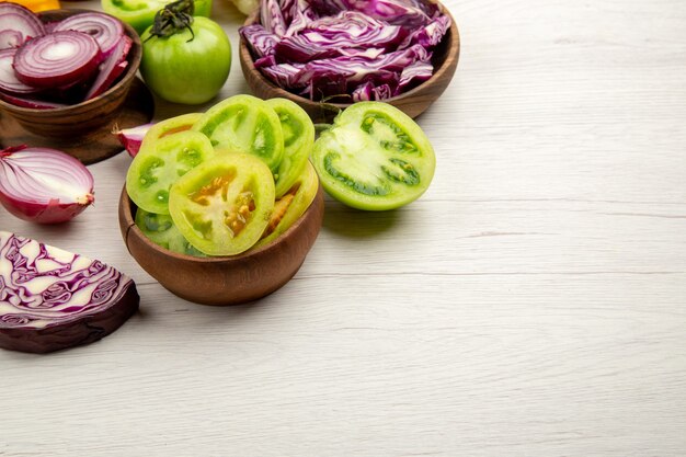 Ansicht von unten frisches Gemüse geschnittene grüne Tomaten geschnitten Rotkohl geschnittene Zwiebel in Schalen auf weißem Holztisch mit freiem Platz