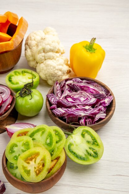 Kostenloses Foto ansicht von unten frisches gemüse geschnittene grüne tomaten geschnitten rotkohl in schalen paprika blumenkohl auf weißem holztisch