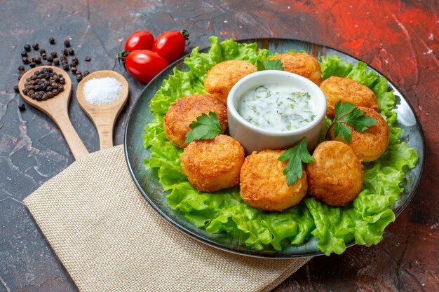 Ansicht von unten gebratene Cheee Balls Salat auf Teller Kirschtomaten Salz und schwarzer Pfeffer in Holzlöffeln auf dunklem Tisch