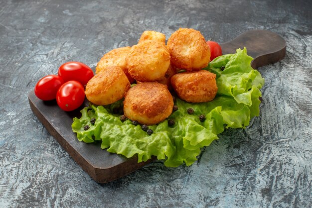 Ansicht von unten gebratene Käsebällchen Kirschtomaten Salat auf Schneidebrett auf grauem Hintergrund