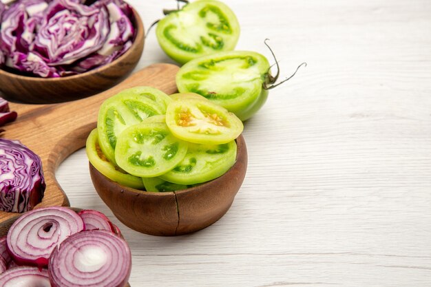 Ansicht von unten gehackter Rotkohl geschnittene Zwiebel geschnittene grüne Tomaten in Schalen auf weißer Oberfläche