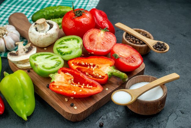 Ansicht von unten Gemüse Pilze Tomaten rote Paprika auf Schneidebrett Knoblauch schwarzer Pfeffer und Salz in Schalen Holzlöffel Gurken auf schwarzem Tisch