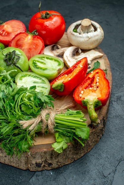 Kostenloses Foto ansicht von unten gemüse tomaten paprika grüns pilz auf holzbrett auf dunklem tisch