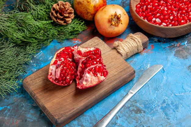 Ansicht von unten Granatapfelkerne in Schüssel Abendessen Messer ein geschnittener Granatapfel auf Schneidebrett Ästen auf Blau