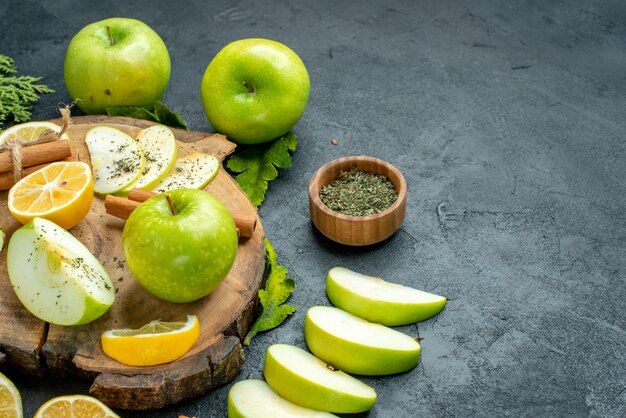 Ansicht von unten grüne Äpfel Zimtstangen und Zitronenscheiben Apfelscheiben auf Holzbrett getrocknetes Minzpulver in kleiner Schüssel auf schwarzem Tisch frei