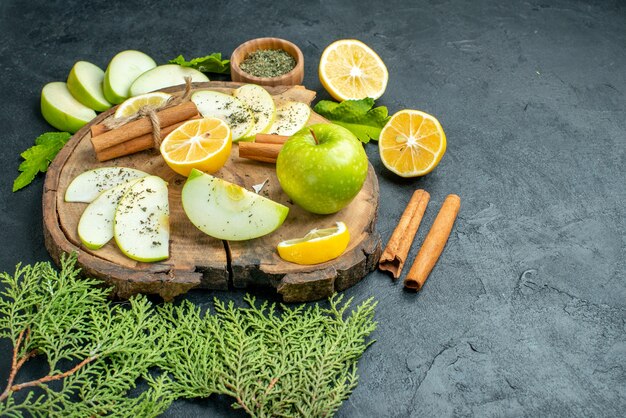 Ansicht von unten grüner Apfel Zimtstangen Apfel- und Zitronenscheiben auf Holzbrett Kiefernzweig in Schüssel auf schwarzem Tisch