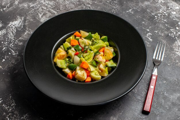 Ansicht von unten grüner Tomatensalat auf ovalem Teller eine Gabel auf dunklem Hintergrund