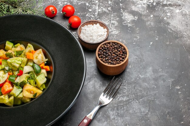 Ansicht von unten grüner Tomatensalat auf ovaler Platte eine Gabel würzt Tomaten auf dunklem Hintergrund