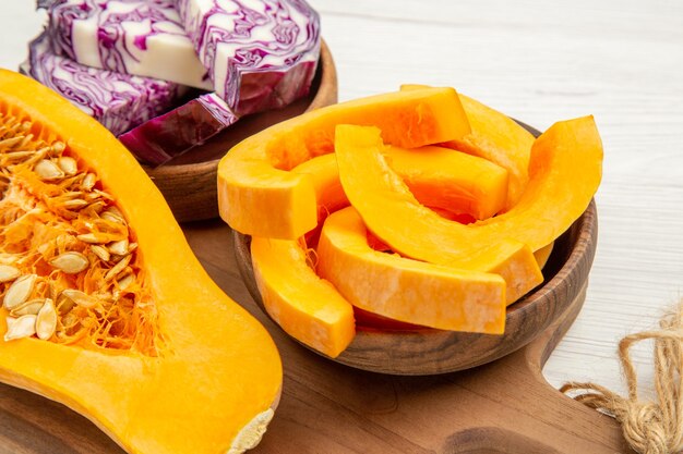 Ansicht von unten halber Butternut-Kürbis Rotkohl und Kürbisscheiben in Schalen auf Schneidebrett auf weißem Tisch