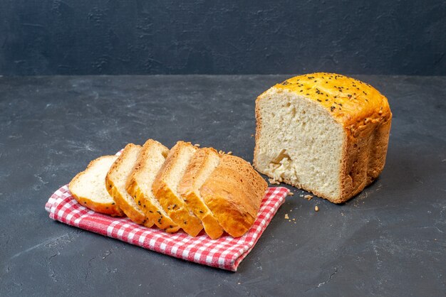 Ansicht von unten halbes Brot und Brotscheiben auf rot-weiß kariertem Küchentuch auf dunklem Tisch