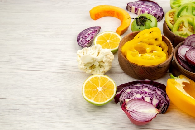 Ansicht von unten Holzschalen mit geschnittenem Gemüse Blumenkohl Zwiebel Rotkohl grüne Tomate gelbe Paprika Zitrone auf weißem Tisch mit freiem Platz