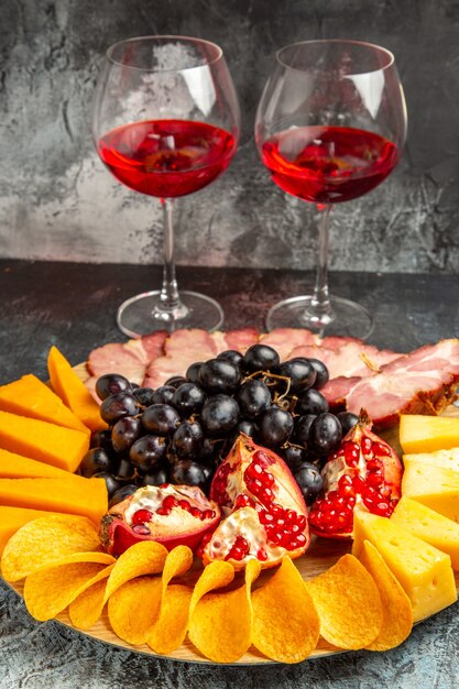 Ansicht von unten Käsestücke Fleischtrauben und Granatapfel auf ovalem Servierbrett Weingläser auf dunklem Hintergrund