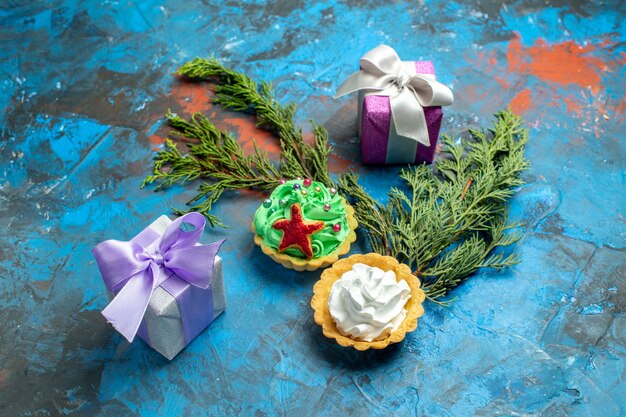 Ansicht von unten kleine Törtchen kleine Geschenke Tannenzweige auf blauroter Oberfläche