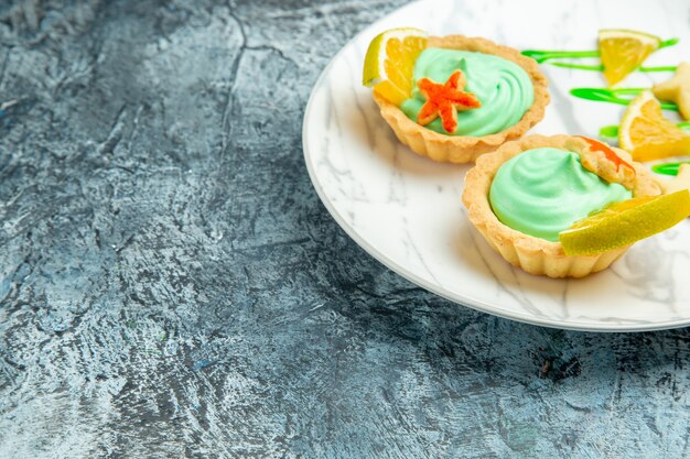 Ansicht von unten kleine Törtchen mit grüner Gebäckcreme und Zitronenscheibe auf Teller auf dunklem, freiem Platz