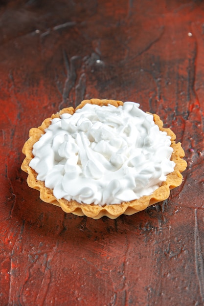 Ansicht von unten kleine Torte mit Gebäckcreme auf dunkelrotem Tischfreiraum