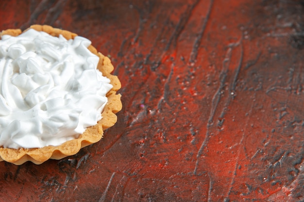 Ansicht von unten kleine Torte mit Gebäckcreme auf dunkelrotem Tischkopierraum