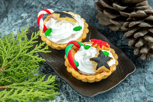 Ansicht von unten kleine Weihnachtstörtchen auf schwarzem Teller Tannenzapfen auf grauem Tisch