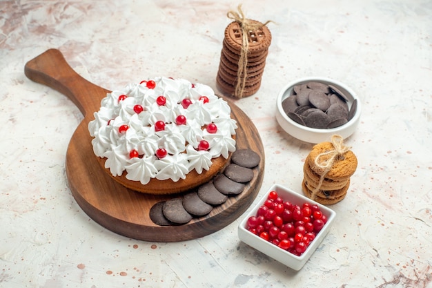 Ansicht von unten kuchen mit weißer creme auf hölzernen schneidebrettschalen mit beeren und schokoladenkeksen, die mit einem seil auf hellgrauem tisch gebunden sind