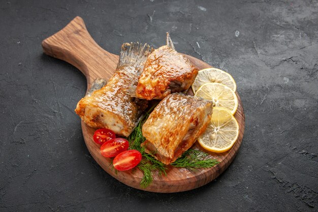 Ansicht von unten leckere Fisch braten Zitronenscheiben schneiden Kirschtomaten auf Schneidebrett auf schwarzem Tisch