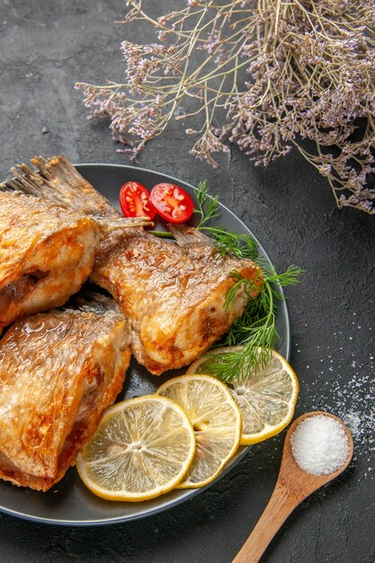 Ansicht von unten leckeren Fisch braten Zitronenscheiben geschnitten Kirschtomaten auf Teller getrockneten Blumenzweig auf schwarzem Tisch