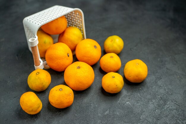 Ansicht von unten Mandarinen und Orangen aus Plastikkorb auf dunklem Hintergrund verstreut