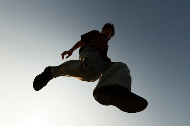 Kostenloses Foto ansicht von unten: mannsilhouette springt bei sonnenuntergang
