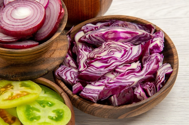 Ansicht von unten schneiden Gemüse geschnitten Rotkohl geschnittene Zwiebel geschnittene grüne Tomaten in Schalen auf weißem Tisch