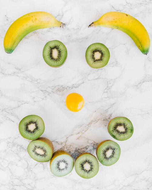 Anthropomorphes Gesicht aus Bananen; Kiwis und Pflaumenfrüchte auf Marmor