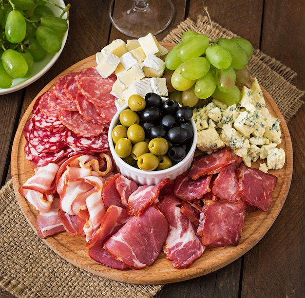 Antipasti Catering Platte mit Speck, Trockenfleisch, Salami, Käse und Trauben auf einem Holztisch