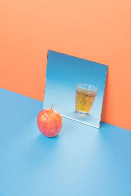 Apfel nahe Glas mit Saft im Spiegel auf blauem Tisch lokalisiert