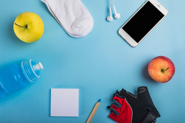 Apfel; Socke; Kopfhörer; Wasserflasche; Haftnotiz; Bleistift; Handschuh und Handy auf blauem Hintergrund