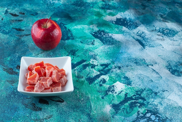 Apfel und rote Marmelade in einer Schüssel auf dem blauen Tisch.