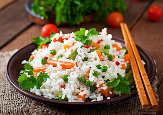 Appetitanregender gesunder Reis mit Gemüse im weißen Teller auf einem Holztisch.