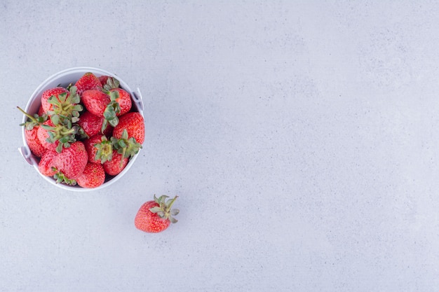 Appetitanregender Haufen Erdbeere in einem kleinen Eimer auf Marmorhintergrund. Foto in hoher Qualität