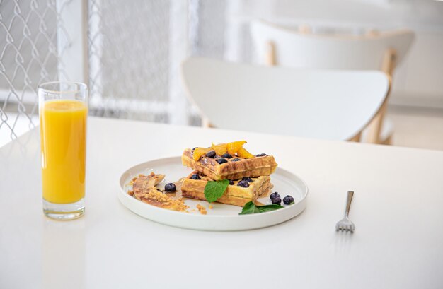 Appetitliche belgische Waffeln mit Beeren und Früchten und einem Glas Saft auf dem Tisch, das Konzept eines köstlichen Frühstücks.