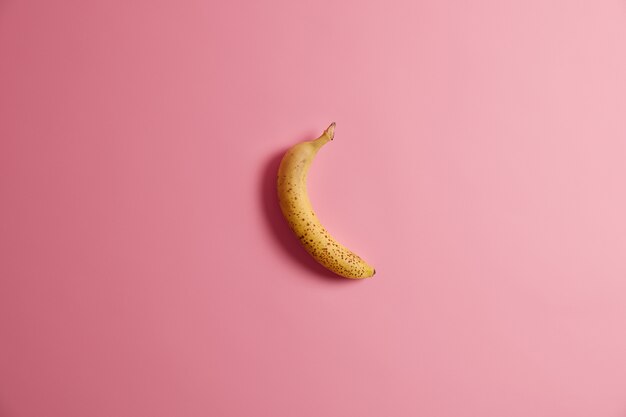 Appetitliche frische ganze gelbe Banane lokalisiert auf rosa Hintergrund. Leckeres ungeschältes Obst zum Frühstück. Horizontale Aufnahme. Reife Früchte mit viel Kalorien und Vitaminen. Sauberes Esskonzept.