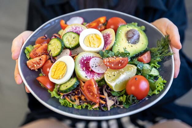 Appetitlicher Salat mit frischem Gemüse und Eiern in einem Teller in weiblichen Händen