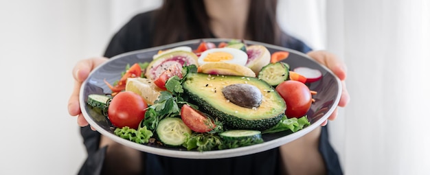 Appetitlicher Salat mit frischem Gemüse und Eiern in einem Teller in weiblichen Händen