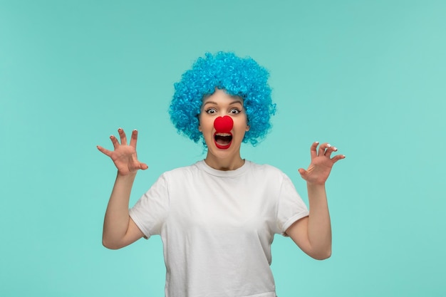 Aprilscherz erschreckendes Mädchen, das Hände mit roter Nase in einem blauen Haar des Clownkostüms fängt