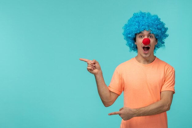 Aprilscherz-Tag-Typ-Clown, unerwarteter Zeigefinger, offener Mund, blaues Haar, aufgeregt, lustige, rote Nase